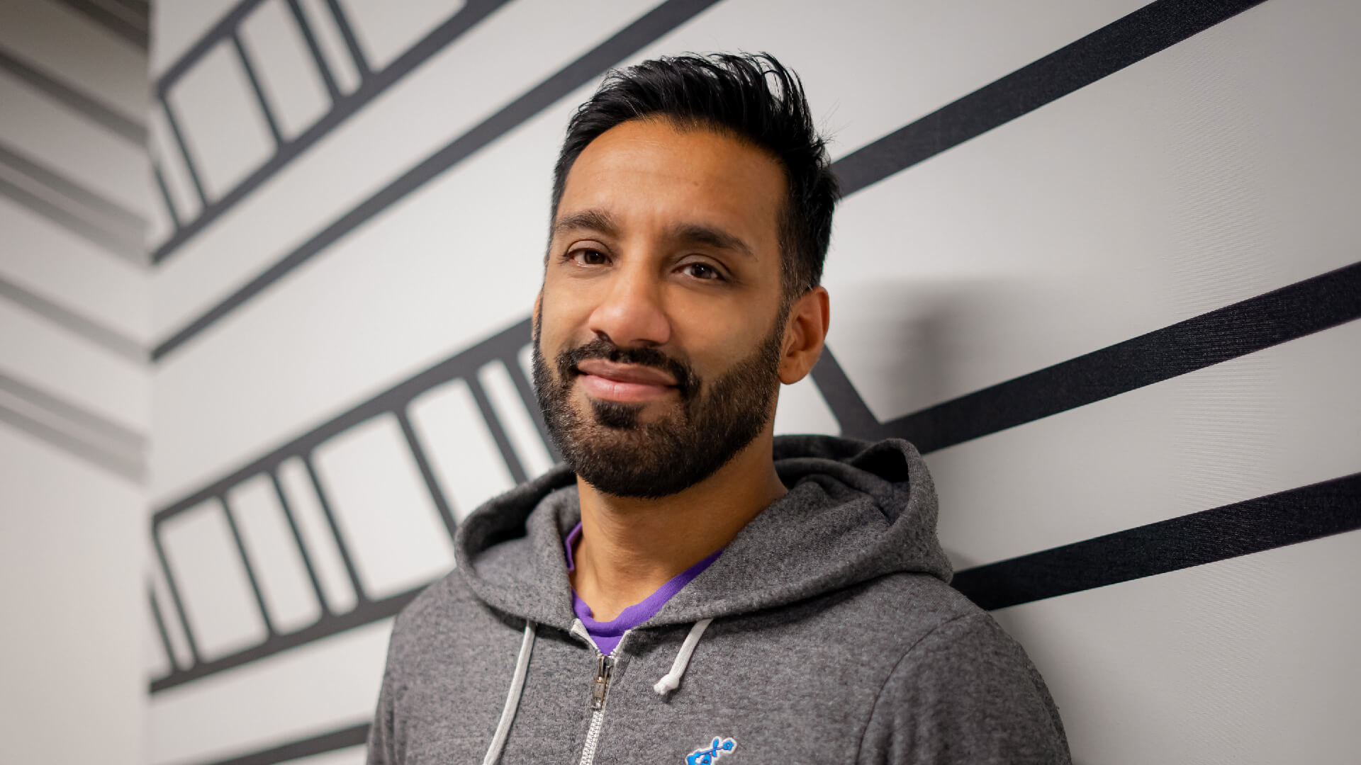A head and shoulders picture of Sagar standing in front of the black and white Escape Studios walls